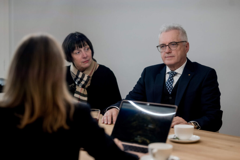 Magdalena Frank sitzt mit Laptop am Tisch im Büro mit zwei Klienten, eine Frau und ein Mann