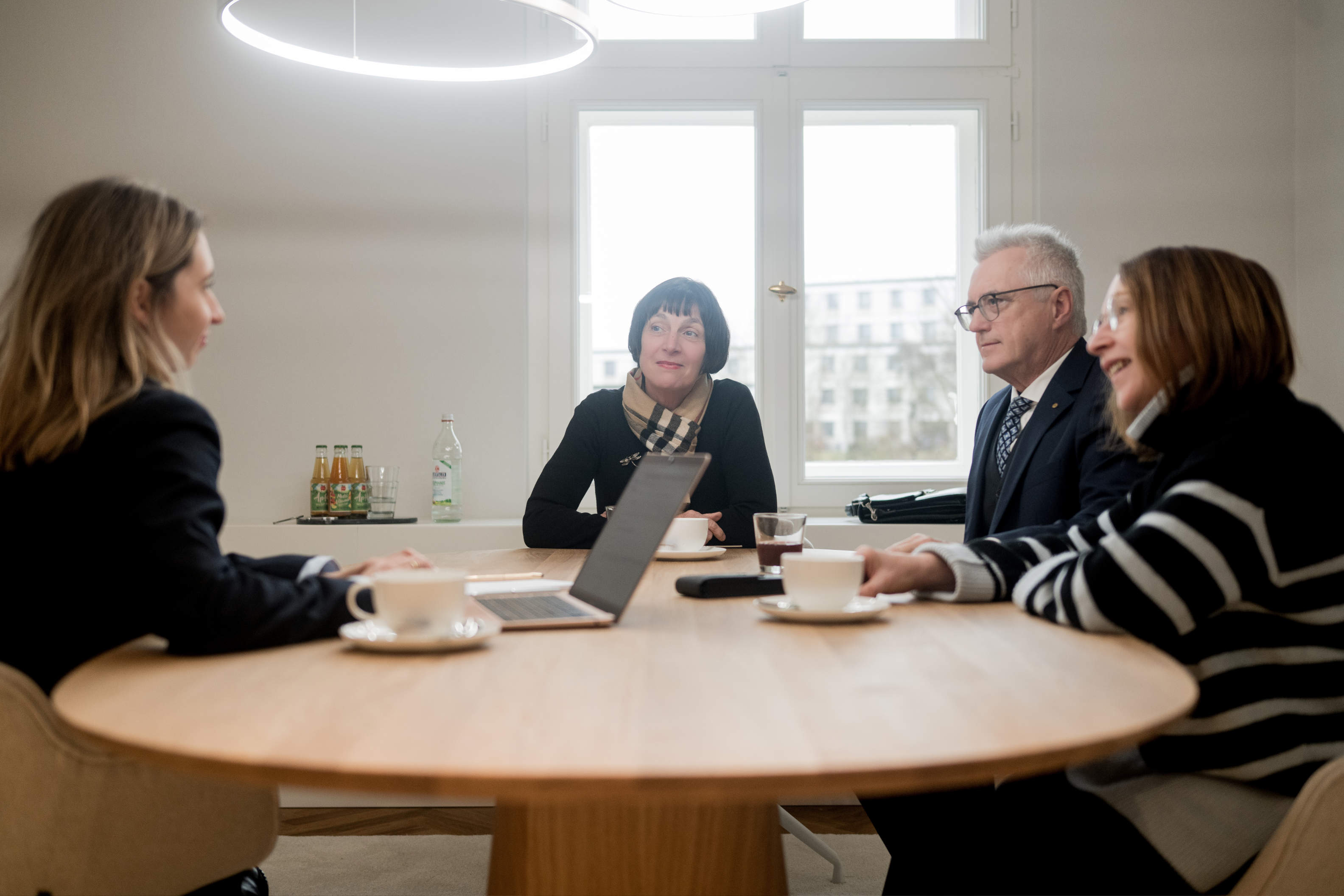 Magdalena Frank sitzt mit Laptop am Tisch im Büro mit drei Klienten, 2 Frauen und ein Mann