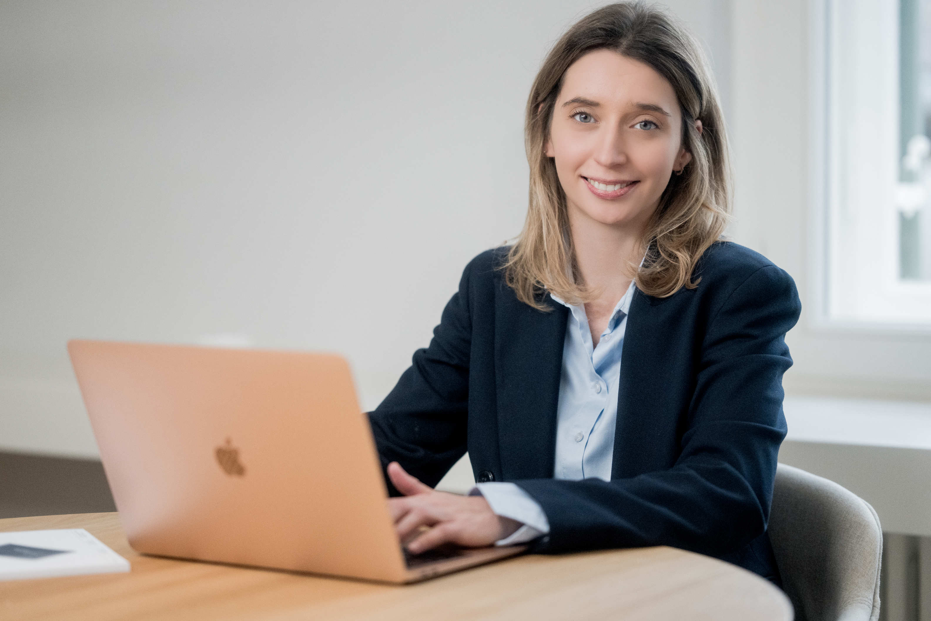 Porträt Magdalena Frank in hellblauer Bluse und dunklem Anzug am Tisch mit Laptop